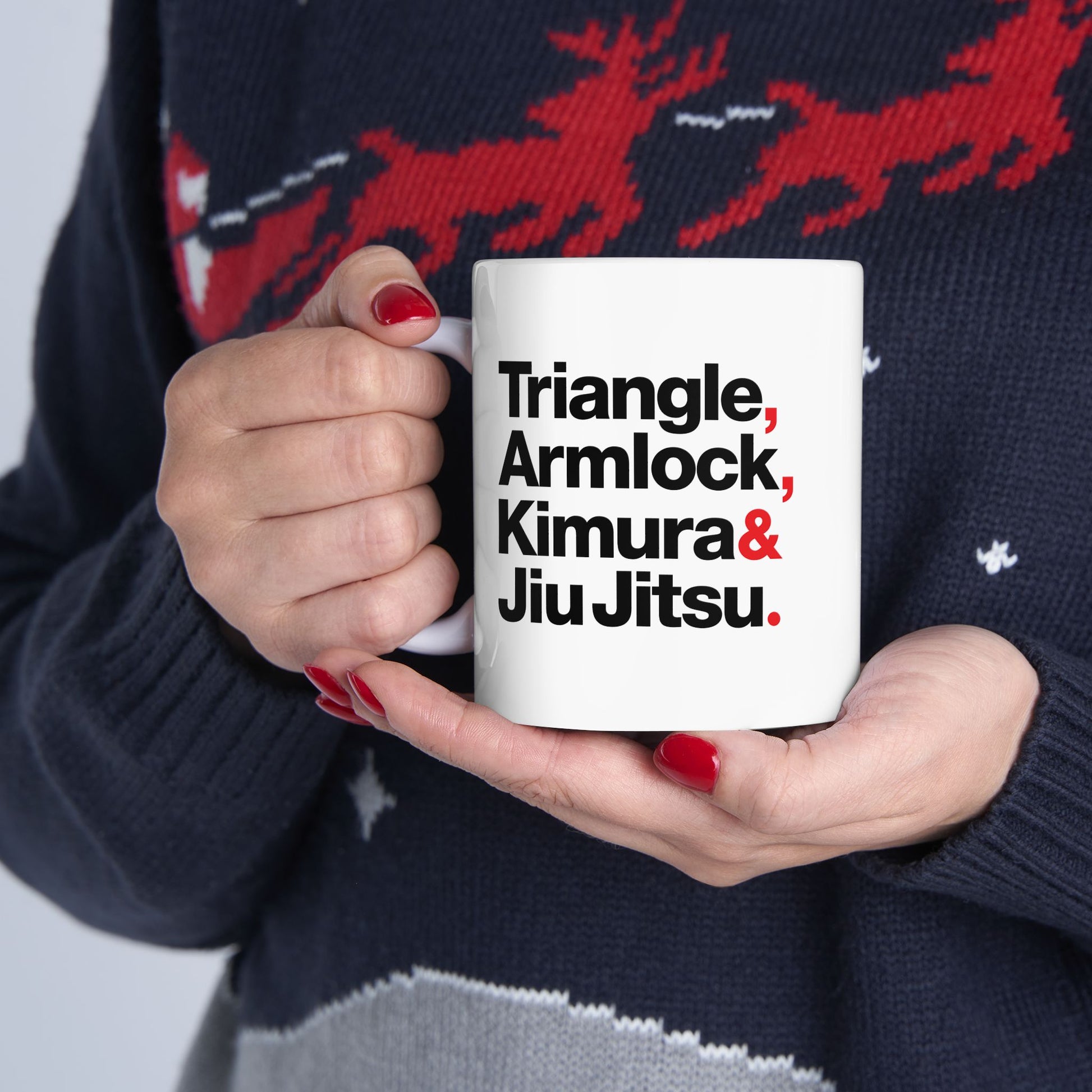 Person holding a mug with martial arts terms text, wearing a dark sweater with red deer design.