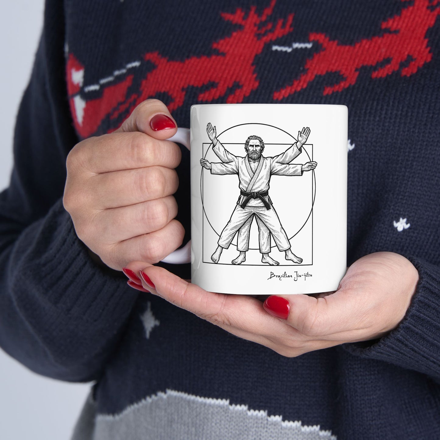 Person holding a mug with a martial arts-themed design against a dark sweater with red deer pattern.