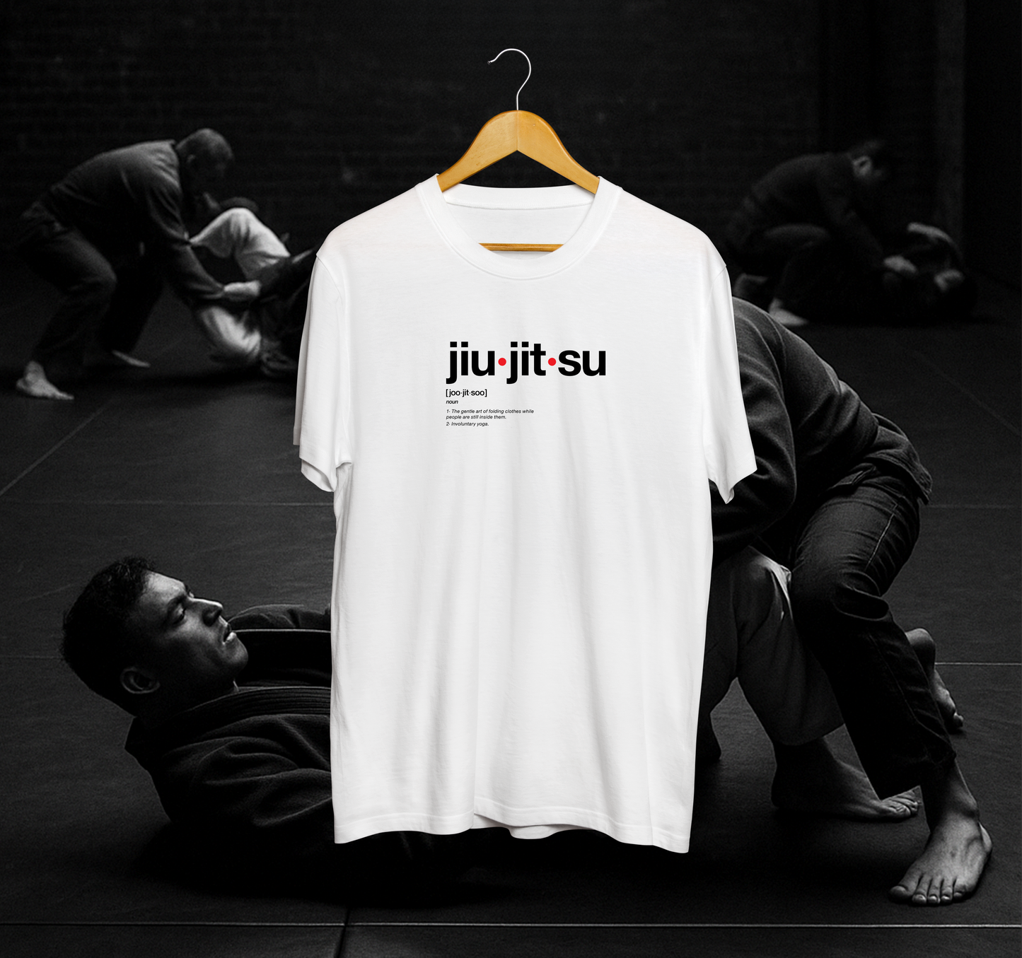 White t-shirt with 'jiu-jitsu' text on a hanger against a black and white background of people practicing martial arts.